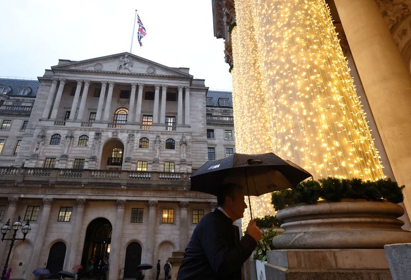 FILE PHOTO: A person shields themselves from the rain while walking near the Bank of England building in London, Britain, December 18, 2025. REUTERS/Toby Melville/File Photo
