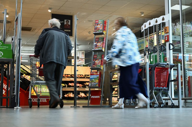 People walk by a flyer stand with a reference to the Europe-wide "true costs" campaign week by the discount supermarket Penny, in which nine selected products are given the calculated "real price" as the sales price, under consideration of the environmental costs, in Berlin, Germany August 1, 2023. REUTERS/Annegret Hilse/File Photo