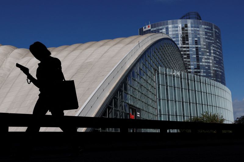 A woman, looking at her mobile phone, walks past buildings at the financial and business district of La Defense in Puteaux near Paris, france, September 12, 2025. REUTERS/Stephanie Lecocq