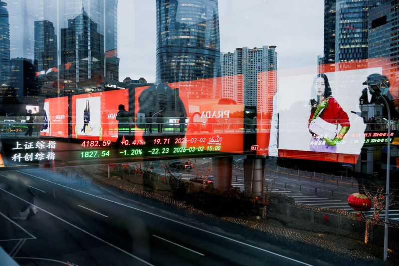 FILE PHOTO: An electronic board shows Shanghai stock indices as people walk on a pedestrian bridge in the Lujiazui financial district in Shanghai, China, March 2, 2026. Picture taken through glass. REUTERS/Go Nakamura/ File Photo