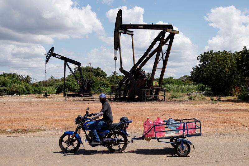 A man on a motorcycle transports water bottles past pumpjacks in Cabimas, Venezuela, January 26, 2026. REUTERS/Leonardo Fernandez Viloria
