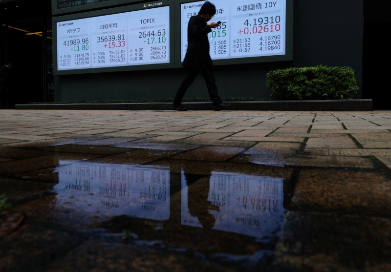 A man walks past a stock quotation board showing the Dow Jones Industrial Average, Nikkei share average, Topix average, Japan and U.S 10-year government bond yield outside a brokerage in Tokyo, Japan April 2, 2025. REUTERS/Kim Kyung-Hoon