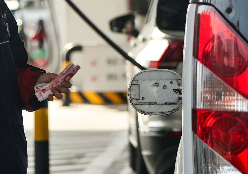 FILE PHOTO: An employee holds Chinese Yuan notes next to an open cap of a car's fuel tank at a gas station ahead of an announced fuel price hike, amid the U.S.-Israeli conflict with Iran, in Beijing, China, March 22, 2026. REUTERS/Maxim Shemetov/File Photo