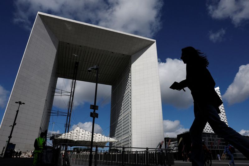 A woman, holding her mobile phone, walks past the Grande Arche at the financial and business district of La Defense in Puteaux near Paris, france, September 12, 2025. REUTERS/Stephanie Lecocq