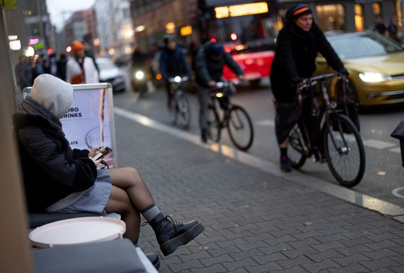 A person sits outside a coffee shop as cyclists and cars make their way on Scheunenviertel quarter in Berlin, Germany, November 15, 2024. REUTERS/Lisi Niesner