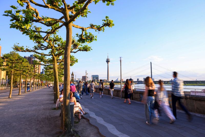 People walk at the promenade by the river Rhine with the skyline in the background including the Rheinturm in Duesseldorf, Germany, May 13, 2024. Picture taken with long exposure. REUTERS/Jana Rodenbusch