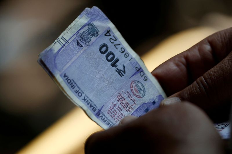 A customer holds hundred rupees Indian currency notes near a roadside currency exchange stall in New Delhi, India, May 24, 2024. REUTERS/Priyanshu Singh