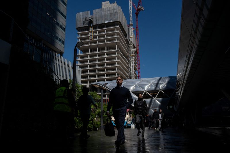 FILE PHOTO: Workers walk through Canary Wharf with a construction site in the background in London, Britain, June 9, 2026. REUTERS/Chris J. Ratcliffe/File Photo