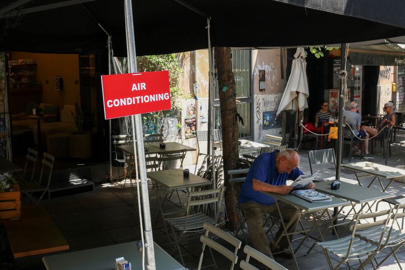 A man reads a newspaper as he sits at a cafe next to an air conditioning sign during a heatwave, in Rome, Italy, June 30, 2026. REUTERS/Guglielmo Mangiapane