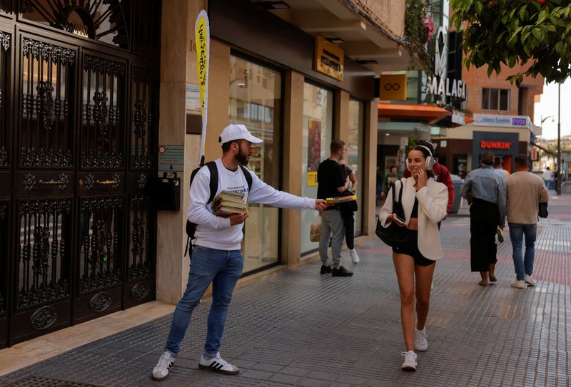 Pedro Moreno, 32, who works on weekends as a waiter and is studying to be a librarian, distributes flyers outside of an optical store, during the working week, in downtown Malaga, Spain, April 1, 2025. REUTERS/Jon Nazca