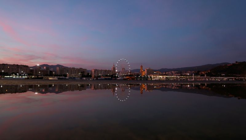 FILE PHOTO: The skyline of the downtown Malaga is seen, reflected in a puddle of water at sunset, from the port of Malaga, southern Spain, October 12, 2018. REUTERS/Jon Nazca/File Photo