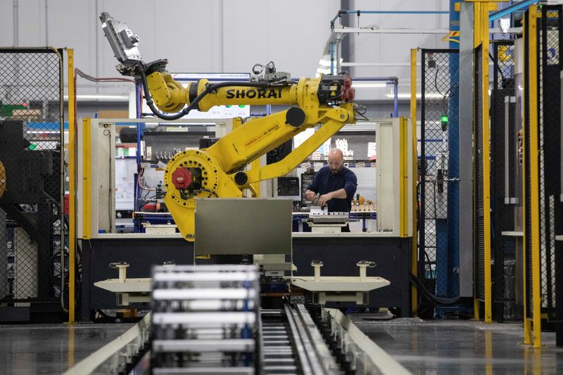 A factory worker works on an aircraft part, as the robot arm of an automated five-axis cell operates autonomously nearby, at Abipa Canada, in Boisbriand, Quebec, Canada May 10, 2023. REUTERS/Evan Buhler