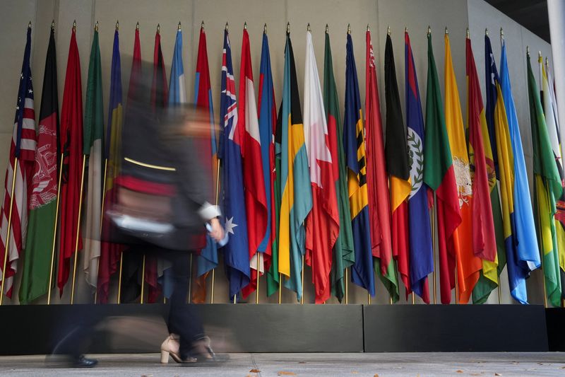 People walk by the flags in front of the IMF building during the IMF/World Bank 2025 Annual Meetings in Washington, D.C., U.S., October 16, 2025. REUTERS/Ken Cedeno