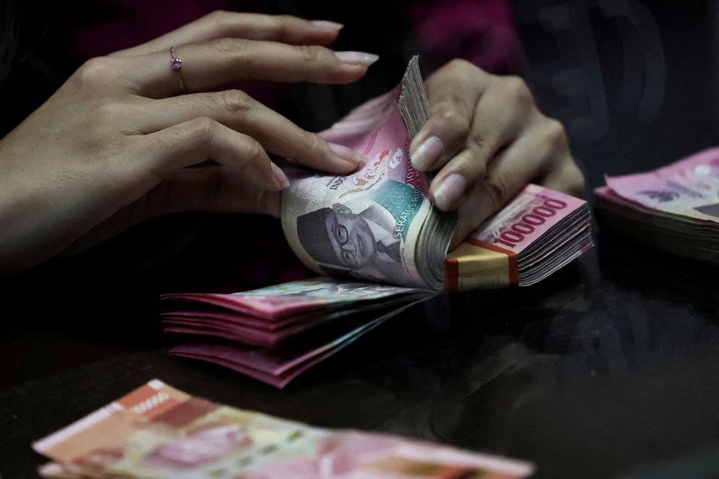 FILE PHOTO: A teller counts rupiah bank notes at a money changer in Jakarta, Indonesia, April 9, 2025. Picture taken through glass. REUTERS/Willy Kurniawan/File Photo