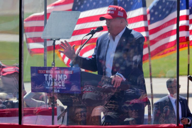 People are reflected in protective glass as they listen to Republican presidential nominee and former U.S. President Donald Trump as he speaks during a rally in Mosinee, Wisconsin, U.S. September 7, 2024. REUTERS/Brian Snyder