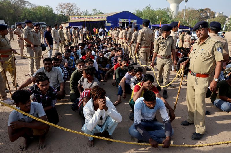 FILE PHOTO: Police officers stand next to men they believe to be undocumented Bangladeshi nationals after they were detained during raids in Ahmedabad, India, April 26, 2025.REUTERS/Amit Dave/File Photo