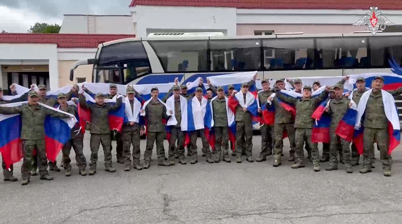 A still image from a video released by the Russian Defence Ministry shows what it said to be Russian service personnel captured by Ukrainian forces and released during the latest exchange of prisoners of war in the course of Russia-Ukraine conflict, as they pose with Russian flags in front of a bus at an unknown location in Belarus, in this image taken from handout footage released June 20, 2025. Russian Defence Ministry/Handout via REUTERS