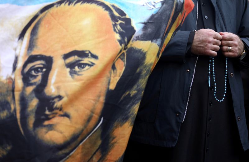 FILE PHOTO: A priest holds a rosary next to a flag with the portrait of late Spanish dictator Francisco Franco outside Mingorrubio-El Pardo cemetery, in Madrid, Spain, October 24, 2019. REUTERS/Sergio Perez/File Photo