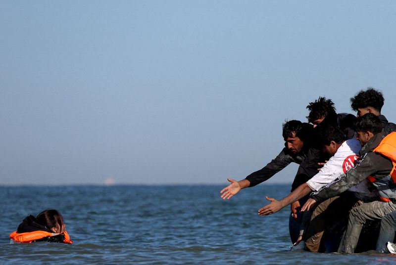FILE PHOTO: A migrant swims to board an inflatable dinghy before leaving the coast of northern France in an attempt to cross the English Channel to reach Britain, from the beach of Petit-Fort-Philippe in Gravelines, near Calais, France, August 25, 2025. REUTERS/Hannah McKay/File Photo