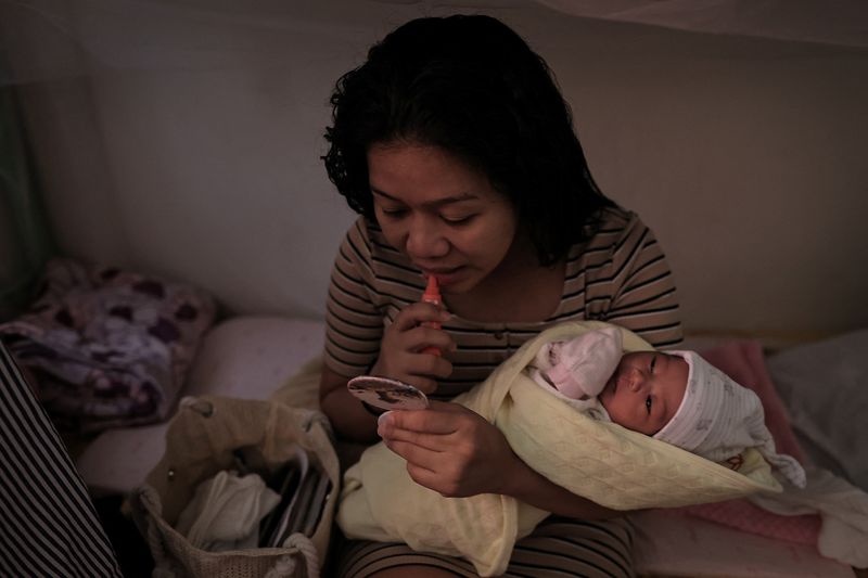 Marian Duhapa, 31, a migrant worker from the Philippines, applies a lip product while holding her newborn daughter, Quinn Dahlia Duhapa, as she prepares to go to the hospital for a routine check in New Taipei City, Taiwan, August 14, 2024. Duhapa had her baby in Taiwan, but after losing her job due to her pregnancy, she had to live in a shelter in New Taipei. As the main breadwinner for her family, she left her daughter at her family home in the Philippines and returned to Taiwan to look for a new job. "I pray for myself, the baby, and my family. I pray I can find a job so I can help my daughter and my family," Duhapa said. "This is my only choice now." REUTERS/Ann Wang        SEARCH "WANG TAIWAN MIGRATION" FOR THIS STORY. SEARCH "WIDER IMAGE" FOR ALL STORIES.