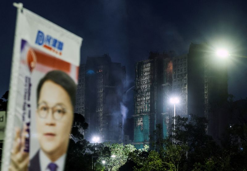 FILE PHOTO: Firefighters work to extinguish a deadly fire at Wang Fuk Court housing complex as a campaign sign for legislator Gary Chan is displayed nearby ahead of the upcoming Legislative Council election, in Hong Kong, China November 27, 2025. REUTERS/Maxim Shemetov/File Photo