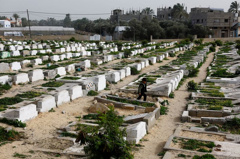 A Palestinian child walks through the cemetery with graves of some of those killed during the war, in Deir al-Balah, central Gaza Strip, January 30, 2026. REUTERS/Mahmoud Issa