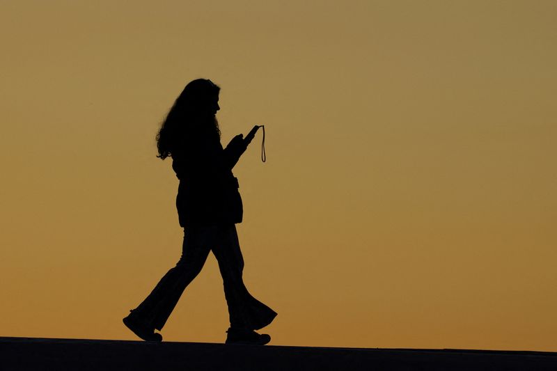 A pedestrian looks at her phone as she crosses a street in Encinitas, California, U.S., January 9, 2024.  REUTERS/Mike Blake