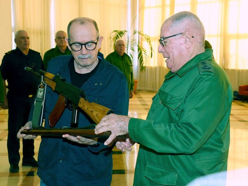 Cuba's folk singer Silvio Rodriguez is presented with an AKM war rifle and a ceremonial replica by Minister of the Revolutionary Armed Forces Army Corps General Alvaro Lopez, in appreciation for a social media post in which he said he was prepared to take up arms against any U.S. invasion, during a ceremony attended by Cuban President Miguel Diaz-Canel at the Ministry of the Revolutionary Armed Forces (MINFAR), in Havana, Cuba, March 20, 2026. Cuba Presidency/Handout via REUTERS