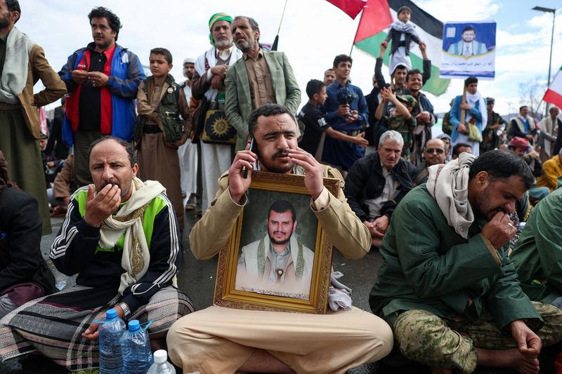 A Houthi supporter holds a poster with an image of the Houthis’s leader, Abdul-Malik al-Houthi, as he speaks on a mobile phone during a demonstration in solidarity with Iran, as the U.S.-Israeli conflict with Iran continues, in Sanaa, Yemen, March 27, 2026. REUTERS/Khaled Abdullah