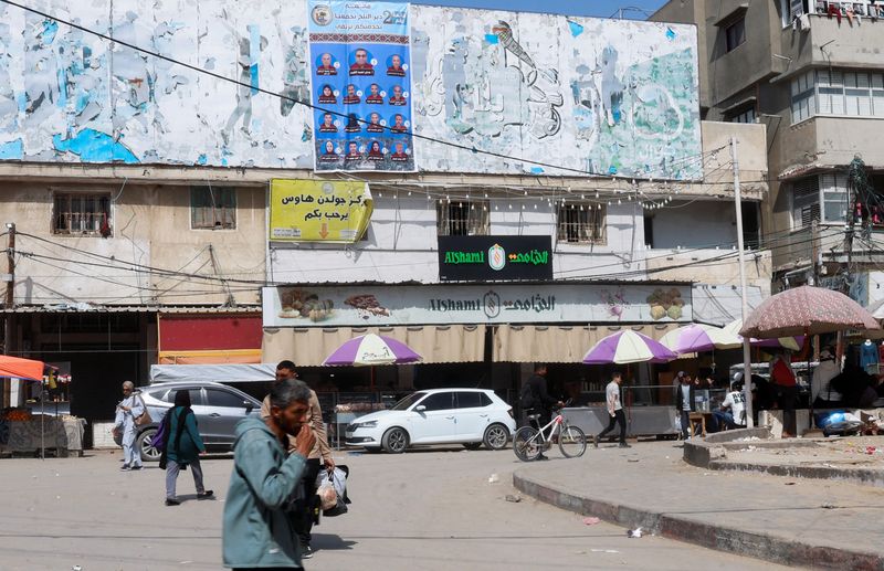 Palestinians walk past an electoral candidates list displayed in Deir al-Balah, central Gaza Strip, April 16, 2026. REUTERS/Haseeb Alwazeer