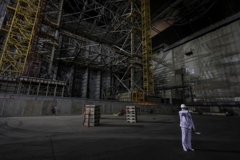 An employee measures a radiation level next to the old sarcophagus covering the damaged fourth reactor, under the New Safe Confinement (NSC) structure at the Chornobyl Nuclear Power Plant, amid Russia's attack on Ukraine, in Kyiv region, Ukraine April 22, 2026. REUTERS/Gleb Garanich
