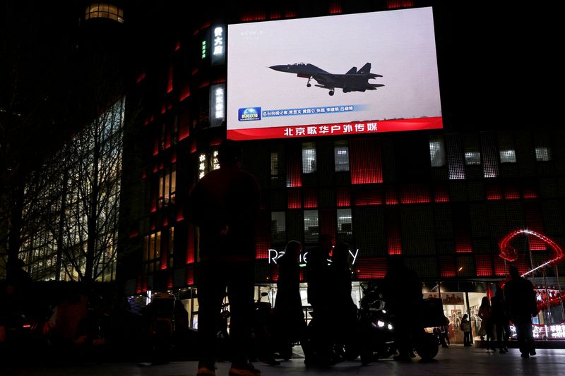 FILE PHOTO: A military aircraft is seen on a giant screen showing news footage about joint army, navy, air and rocket forces drills around Taiwan by the Chinese People's Liberation Army (PLA), outside a shopping mall in Beijing, China, April 1, 2025. REUTERS/Florence Lo/File Photo