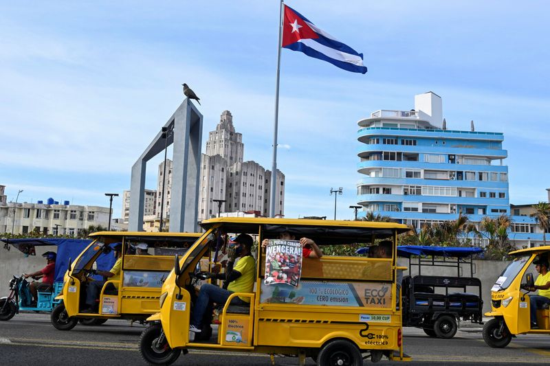 A person riding in electric vehicle carries a sign with an image of late Cuban President Fidel Castro that reads, “The Cuban people shall win” during an anti-imperialist march amid a months-long energy crisis since U.S. President Donald Trump's administration cut off its fuel supply, Havana, Cuba, April 2, 2026. REUTERS/Norlys Perez