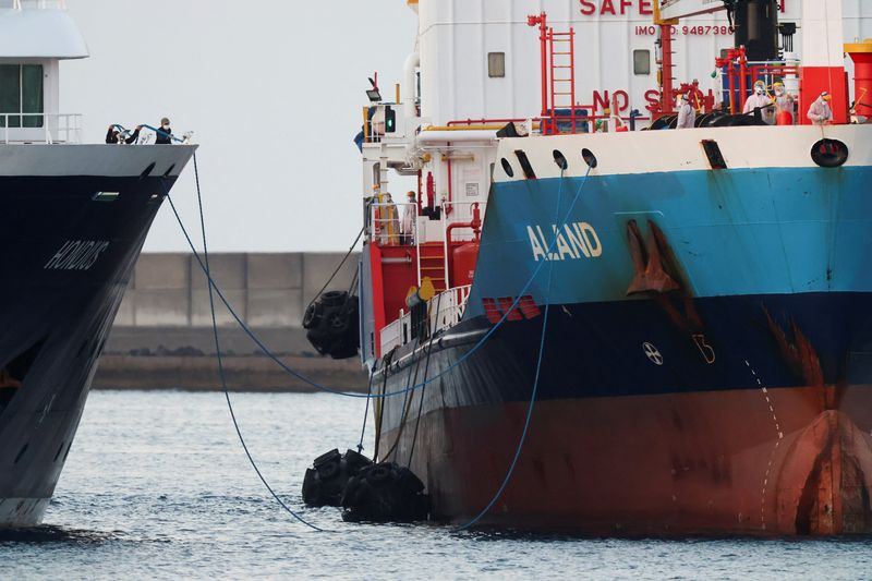 Workers in personal protective equipment (PPE) stand aboard a tanker next to the cruise ship MV Hondius,  affected by a hantavirus outbreak, at the port of Granadilla de Abona, in Tenerife, Spain, May 11, 2026. REUTERS/Hannah McKay