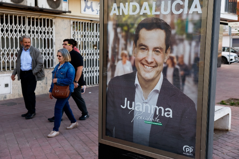 People walk past an electoral poster of Andalusian regional president and People's Party (PP) candidate, Juanma Moreno Bonilla, during the Andalusian regional elections in Ronda, Spain May 17, 2026. REUTERS/Jon Nazca