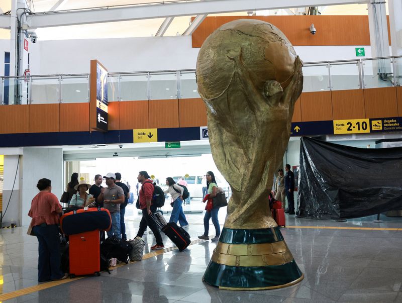 Passengers stand beside a giant replica of the World Cup trophy displayed at Mexico City International Airport, ahead of the World Cup starting on June 11, in Mexico City, Mexico, May 15, 2026. REUTERS/Henry Romero