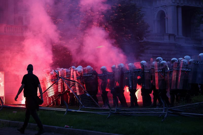 A demonstrator walks near riot police, as a flare emits smoke, during a student-led protest demanding snap parliamentary elections, as Serbia's anti-corruption movement enters a new phase, following the Novi Sad railway station canopy collapse that killed 16 people in 2024, in Belgrade, Serbia, May 23, 2026. REUTERS/Zorana Jevtic