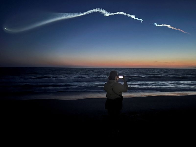 FILE PHOTO: A person takes photos of a trail as the Falcon 9 carrying Starlink satellites streaks across the sky in the latest SpaceX launch as viewed from Venice Beach in Los Angeles, California, U.S., April 6, 2026.   REUTERS/Daina Beth Solomon/File Photo