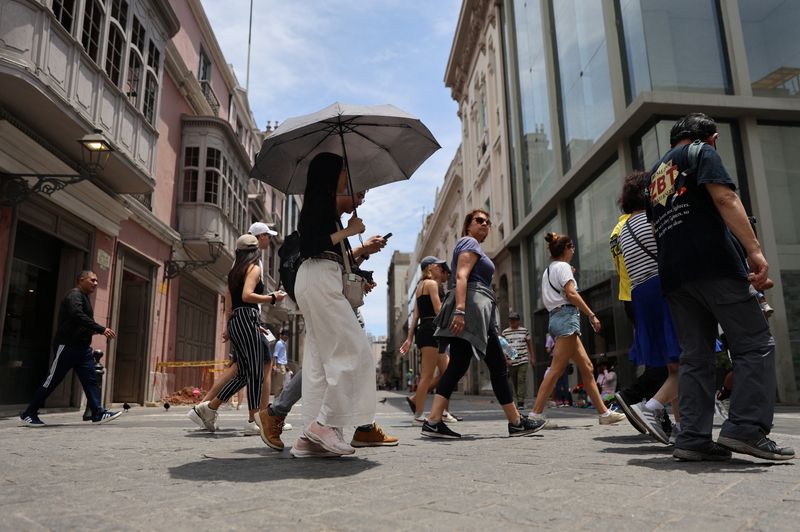 A woman walks through the streets of the downtown with an umbrella due to high temperatures, in Lima, Peru, February 25, 2024. REUTERS/Sebastian Castaneda