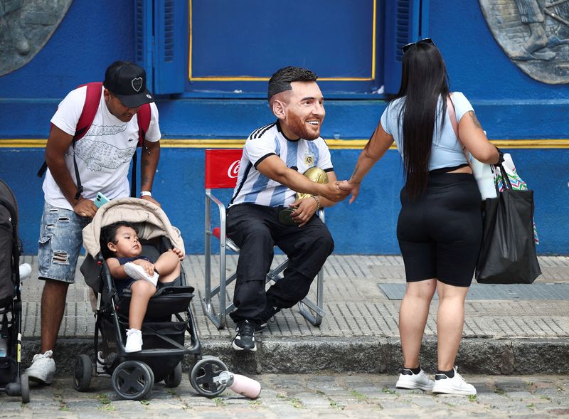 FILE PHOTO: A man wearing a mask depicting Argentine soccer star Lionel Messi, greets a woman as he holds a replica of the FIFA World Cup trophy, ahead the FIFA World Cup draw, in Caminito, Buenos Aires, Argentina December 5, 2025. REUTERS/Agustin Marcarian/File Photo