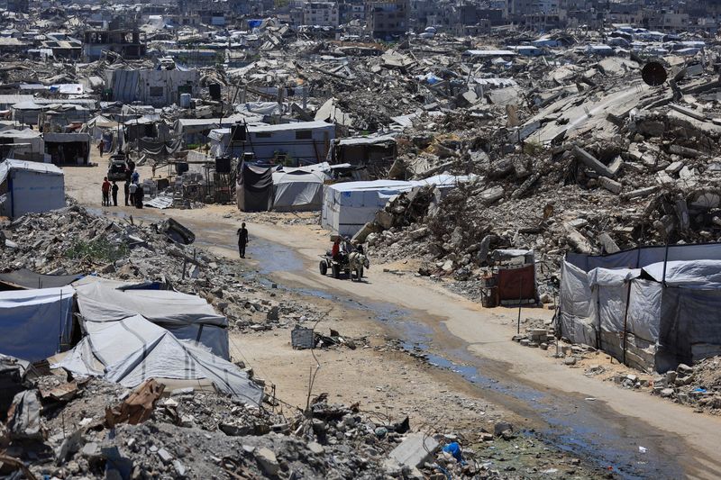 Palestinians make their way past the rubble of residential buildings destroyed during the Israeli offensive as displaced people shelter in tents, in Gaza City, June 15, 2026. REUTERS/Dawoud Abu Alkas