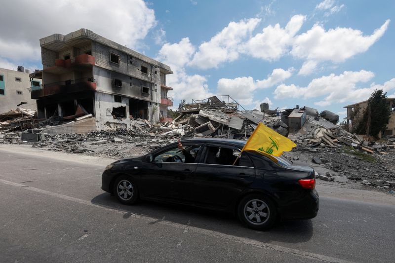 People display a Hezbollah flag from inside a car driving past rubble of destroyed buildings in Deir Qanoun al-Nahr, Tyre district, southern Lebanon,  June 15, 2026. REUTERS/Aziz Taher