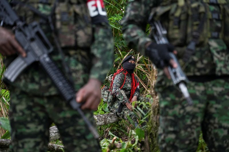 A rebel from Colombia's National Liberation Army (ELN) sits on a tree trunk as fellow rebels stand nearby, in the Choco department, Colombia, June 12, 2026. REUTERS/Jair Coll