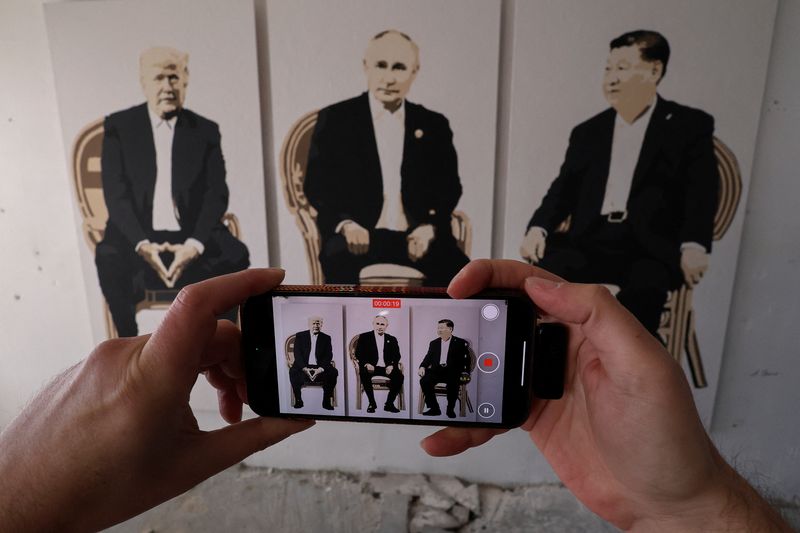 A visitor takes a video of an artwork depicting U.S. President Donald Trump, Russian President Vladimir Putin and Chinese President Xi Jinping at an exhibition, which is called "Yalta 2.0" and opened to make a reference to the 1945 Yalta Conference, at an art gallery in Livadia park in Yalta, Crimea, February 8, 2025. REUTERS/Alexey Pavlishak