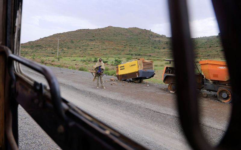 A Tigrayan Militia member stands next to construction machinery destroyed during the fighting between the Tigray People's Liberation Front (TPLF) and Ethiopian National Defence Force (ENDF) allied with Amhara Special Forces and Eritrean Defence Forces (EDF) on the outskirts of Samre, Tigray Region, Ethiopia, June 23, 2023. REUTERS/Tiksa Negeri
