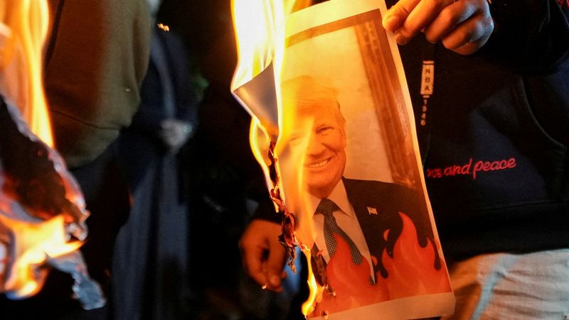 FILE PHOTO: Supporters of Iraqi Shi'ite armed groups burn an image of U.S. President Donald Trump during a rally in solidarity with Iran's government in Tehran, outside the Iranian consulate in Basra, Iraq, January 13, 2026. REUTERS/Mohammed Aty/File Photo