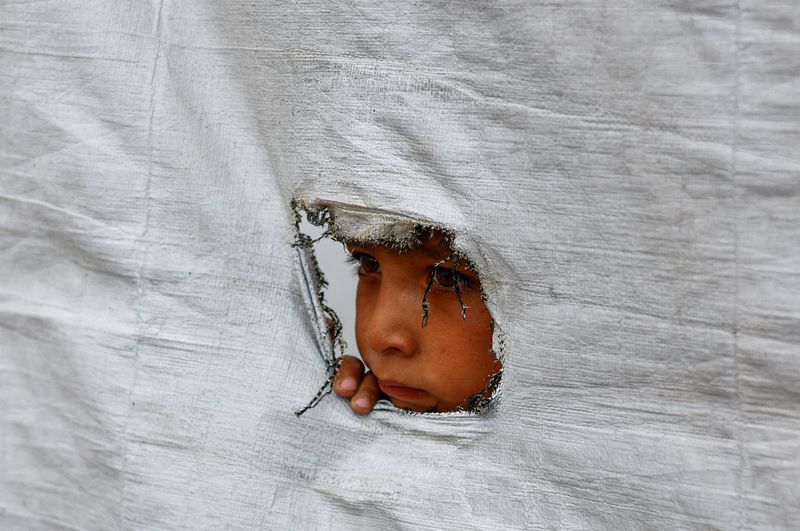 FILE PHOTO: A displaced Palestinian boy peers through a tear in a tent wall, in Gaza City, May 6, 2026. REUTERS/Mahmoud Issa/ File Photo