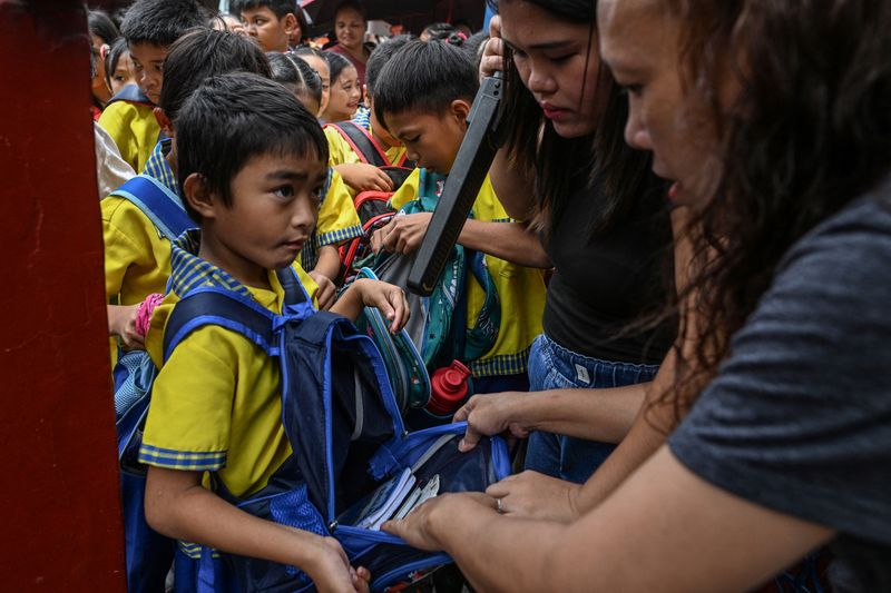 A parent assists in the checking of students' bags as they enter President Corazon Aquino Elementary School, a day after at least three students were killed and seven others injured when two students, aged 15 and 14, opened fire at a school in the city of Tacloban southeast of Manila, in Quezon City, Philippines, June 23, 2026. REUTERS/NOEL CELIS