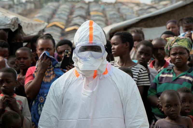 A health worker in personal protective equipment (PPE) stands near displaced people waiting for the burial of suspected Ebola victims at the Kigonze displaced persons camp, in Bunia, eastern Democratic Republic of Congo, June 18, 2026. REUTERS/Gradel Muyisa Mumbere
