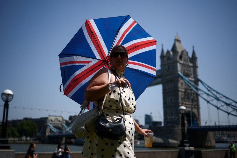 A woman uses an umbrella to shield herself from the sun while walking near Tower Bridge as Britain experiences record temperatures disrupting schools and transport networks, in London, Britain, June 25, 2026. REUTERS/Guglielmo Mangiapane